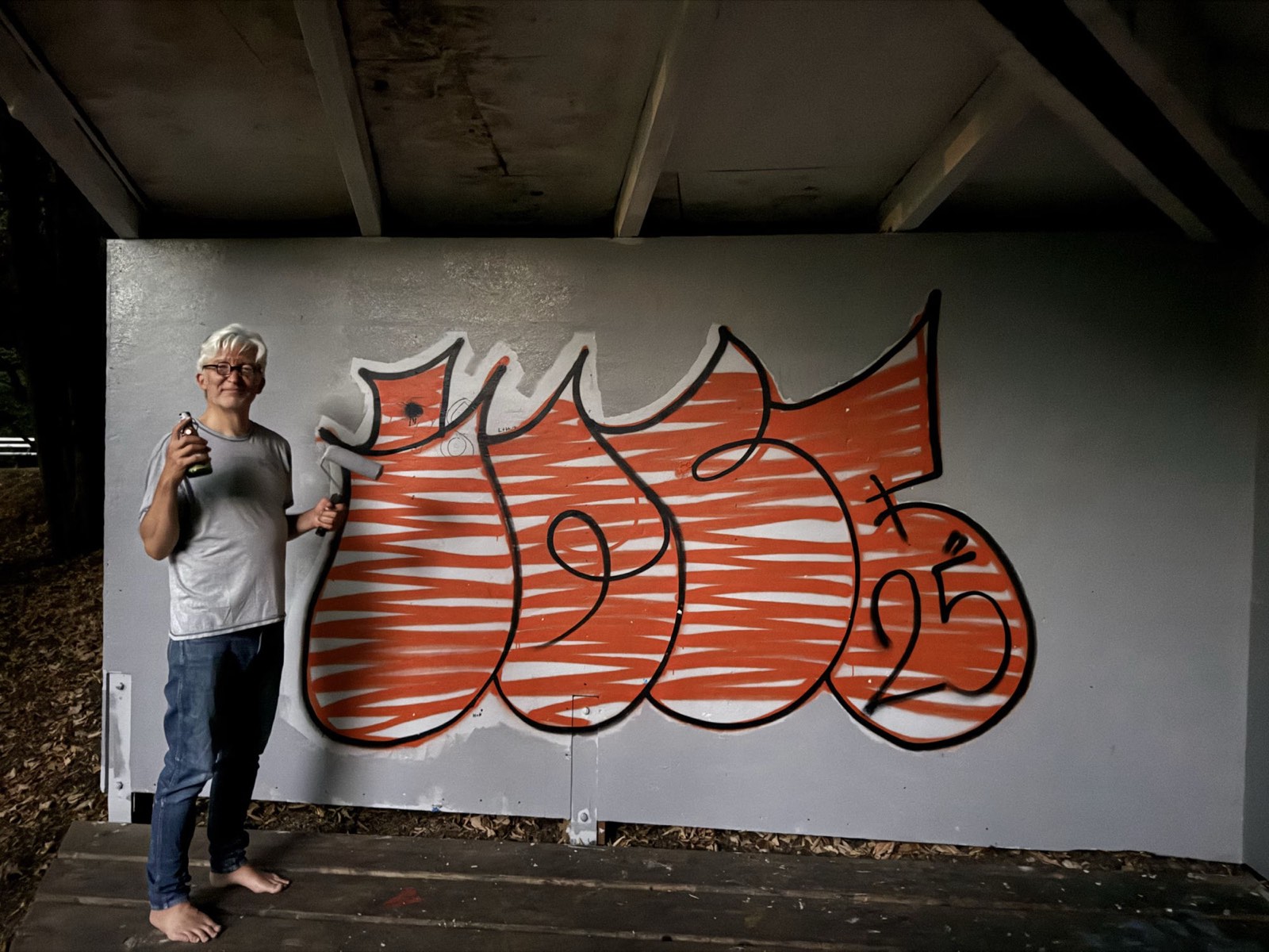 Mark mit Farbrolle und Feierabendbier vor dem freigestellten orangenen Graffiti