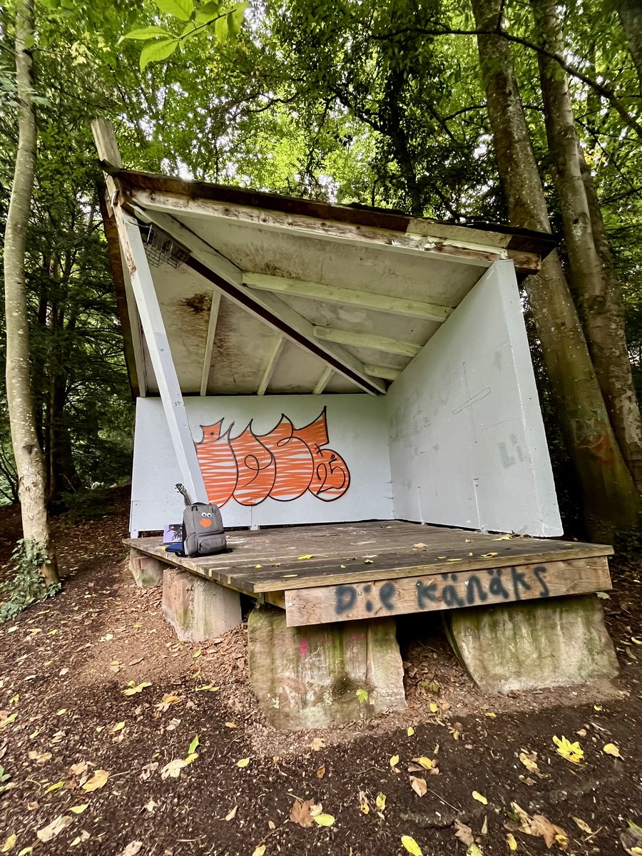 Hütte im Park der Zeiten vor der Grundierung: orangenes Graffiti zwischen neuen Schmierereien